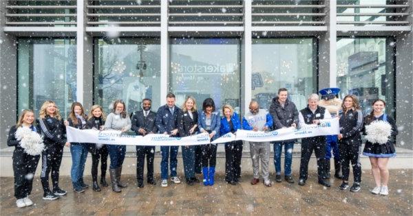 Large snowflakes fall during a ribbon cutting ceremony outside a glass storefront. 