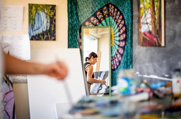 A college student is reflected in a mirror as she paints. 